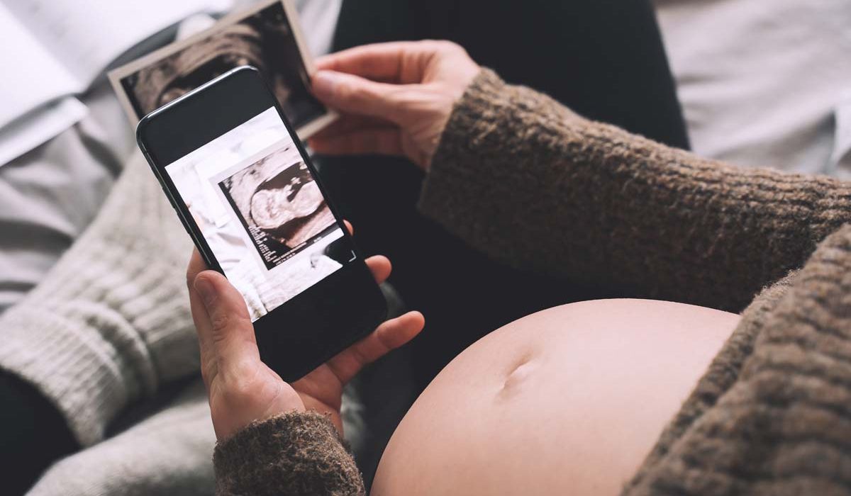 A doctor examines a pregnant woman's abdomen during a prenatal check-up in a clinical setting.